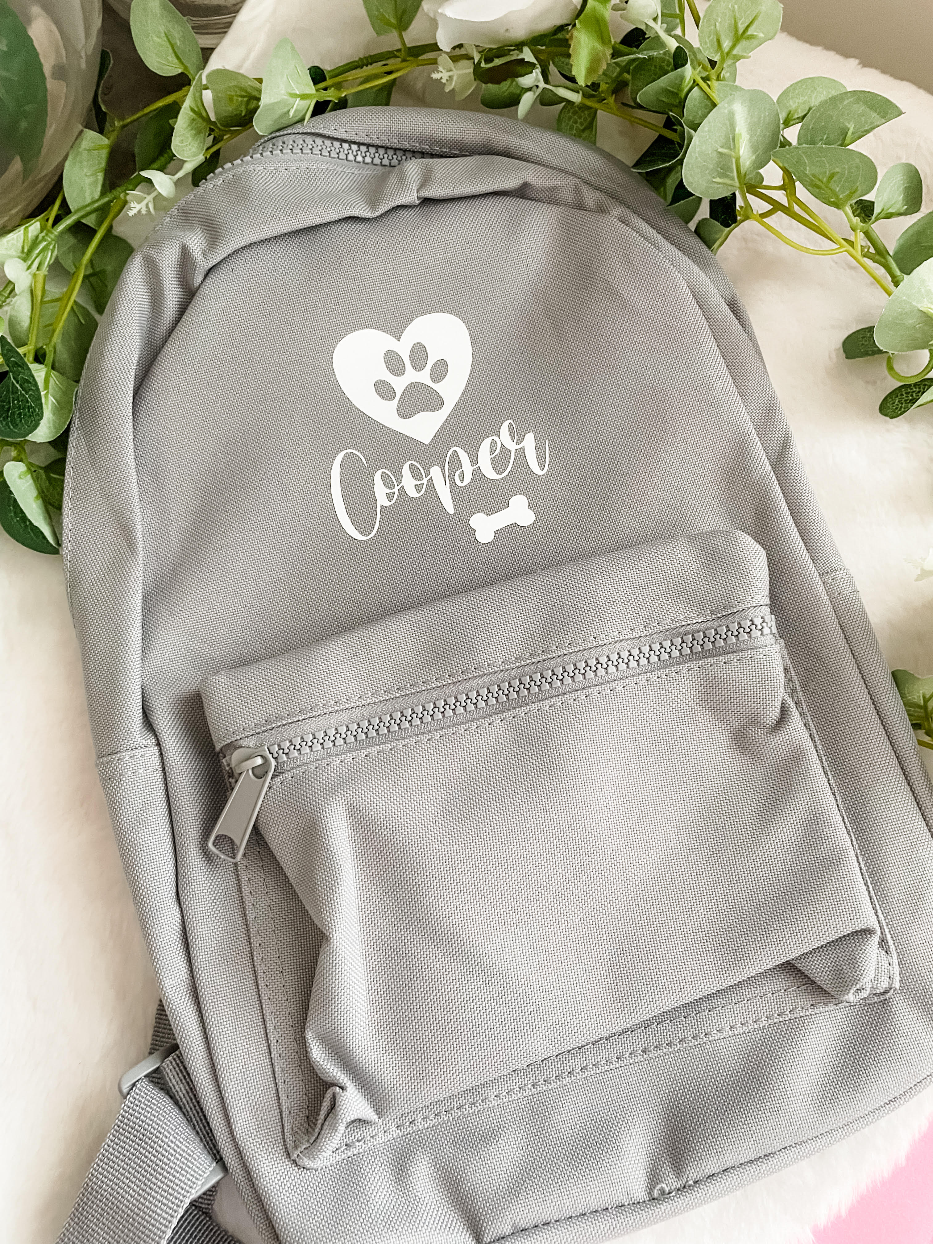 Grey personalised dog backpack laid flat showing custom dog name design with heart, paw print and bone. Custom dog travel bag.