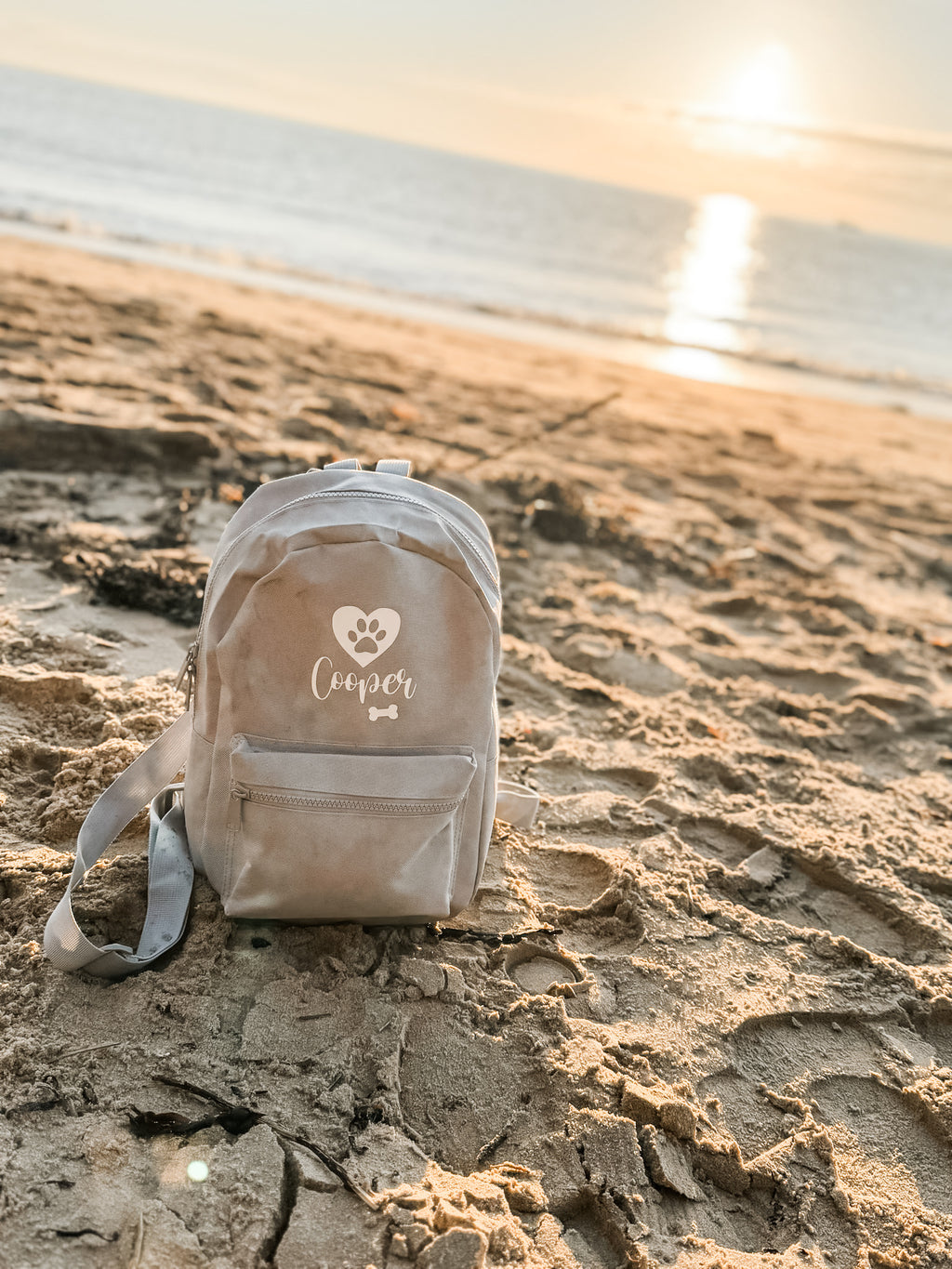 Grey personalised dog backpack displayed on the beach, perfect for carrying dog walking essentials.