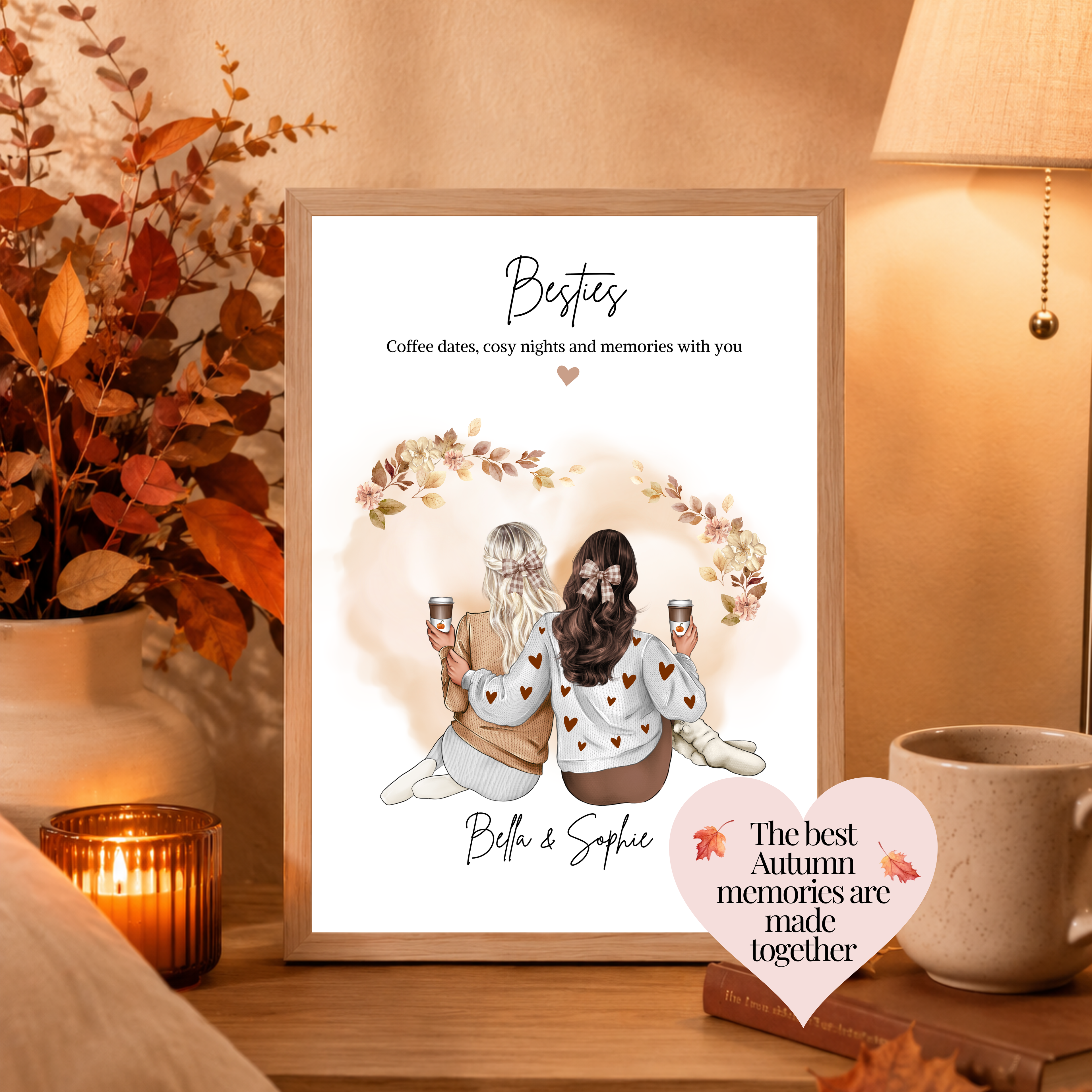 A framed personalised autumn print displayed on a wooden table in a cosy room setting. The print features an illustration of two women holding coffee cups under the heading 'Besties' with the text 'coffee dates, cosy nights and memories with you' both women wearing cosy outfits and brown hair bows. Custom autumn lover gift.