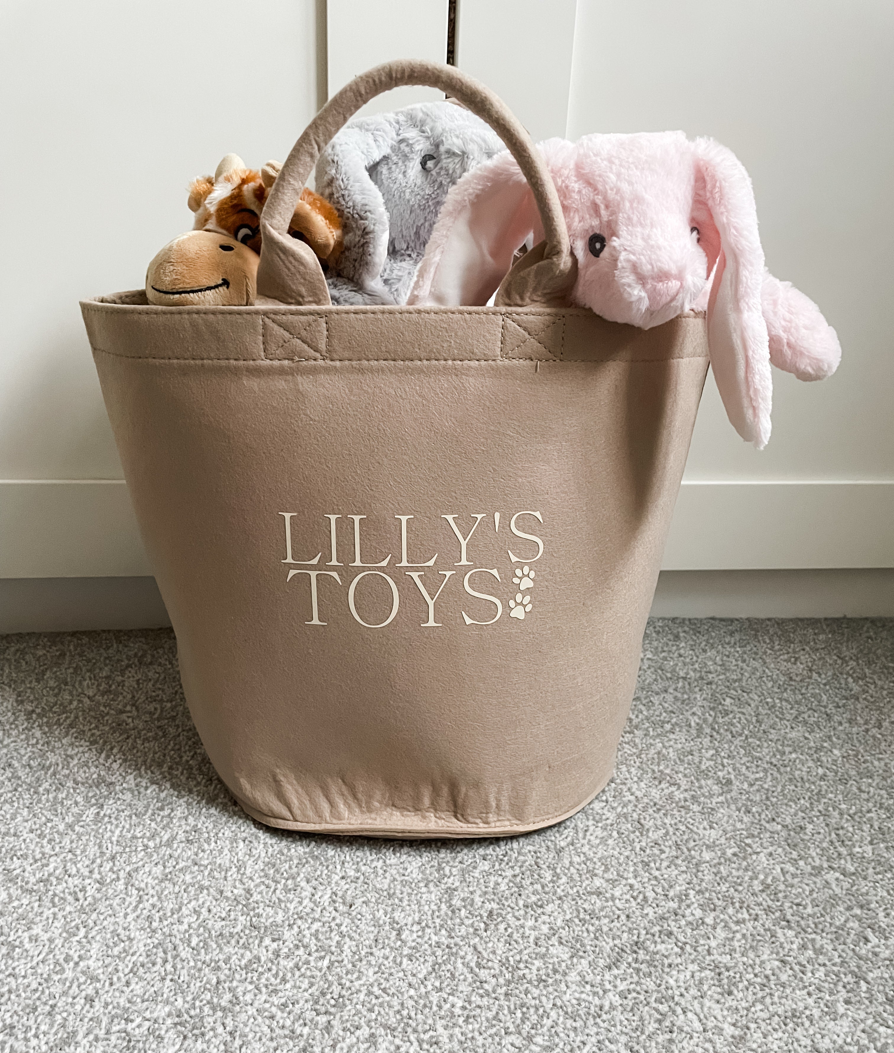 Personalised sand felt dog toy storage basket filled with plush dog toys in a cosy home.