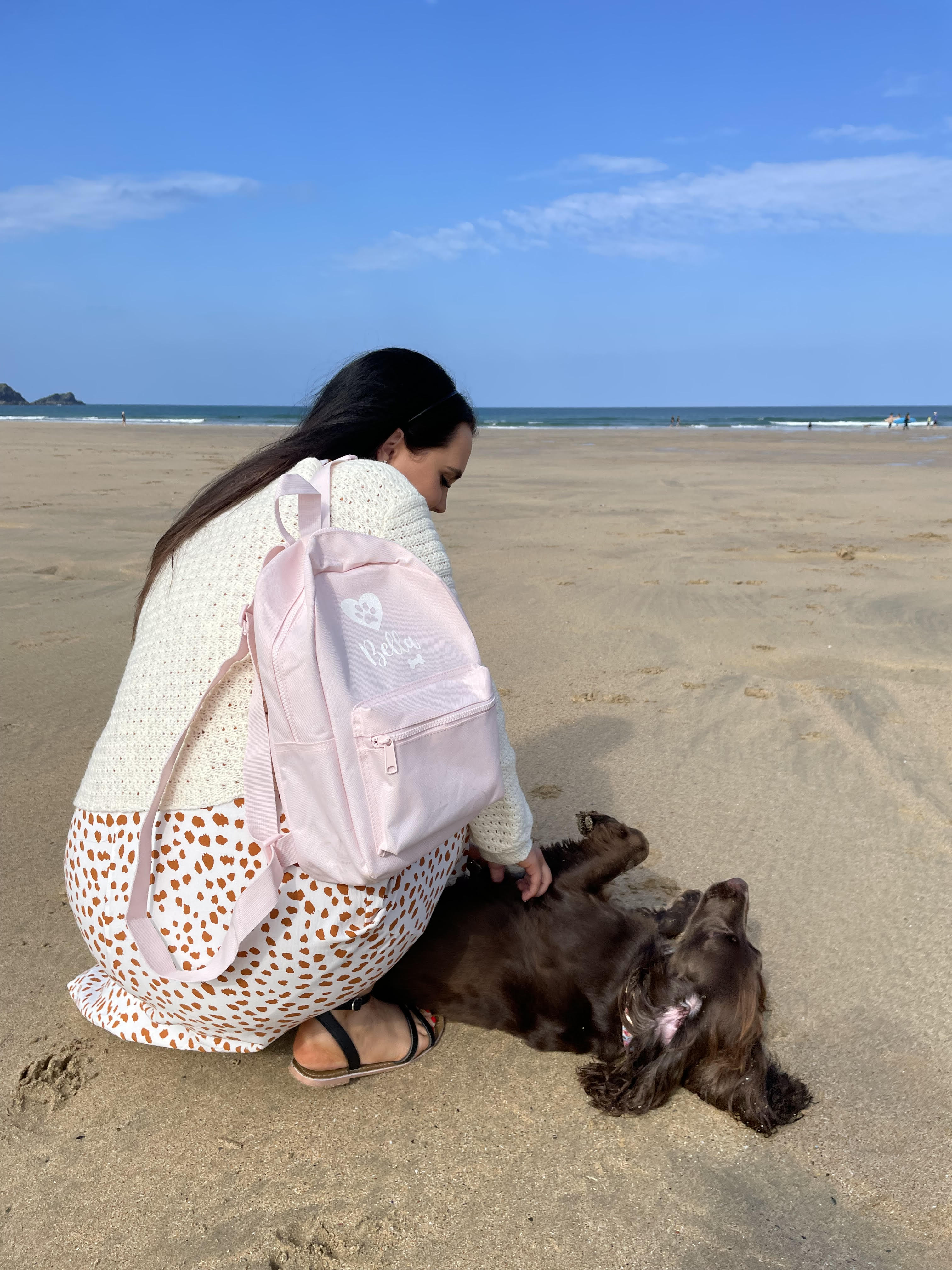 Personalised pink dog walking backpack with custom dog name, carried at the beach beside a Cocker Spaniel.