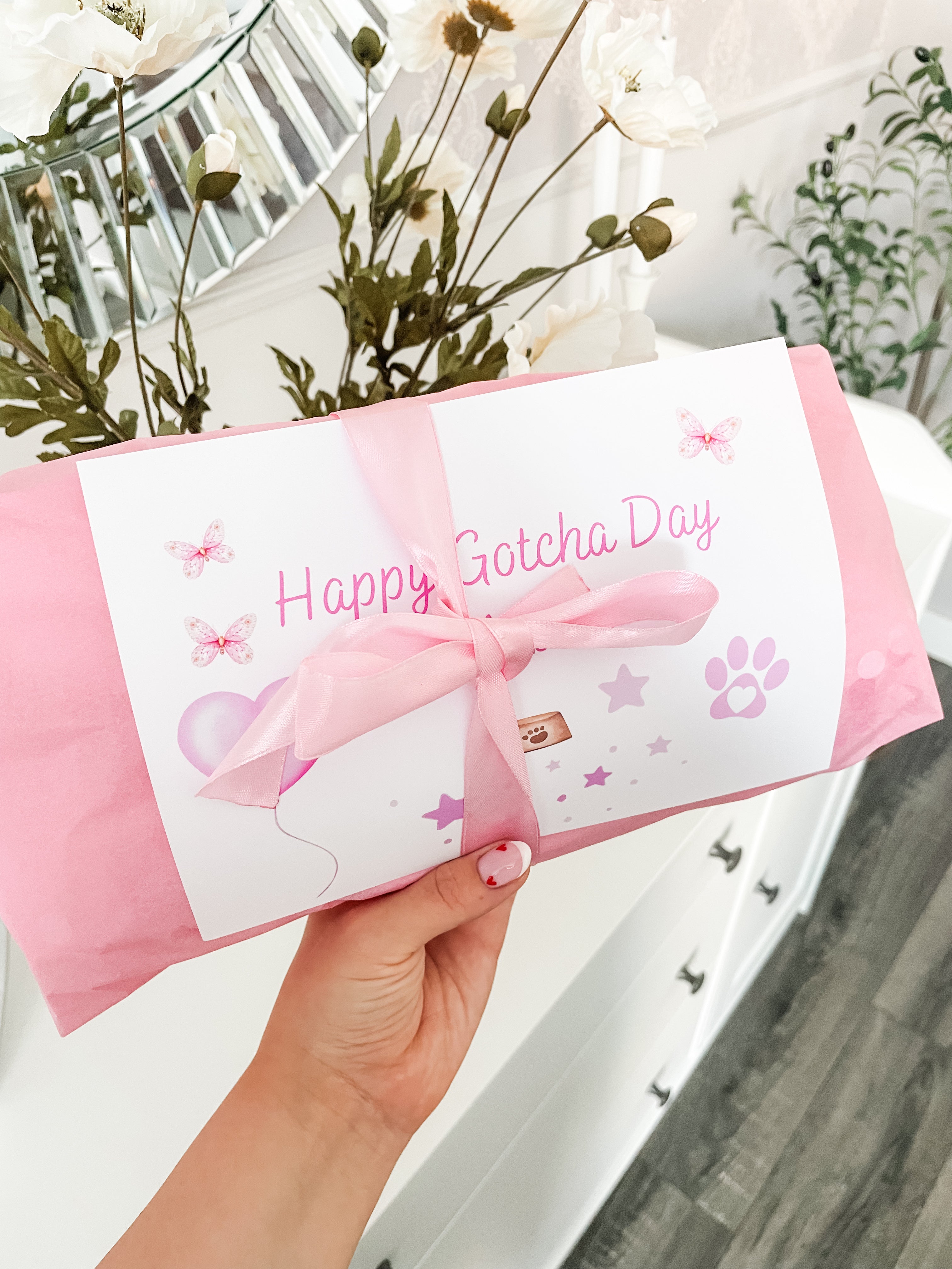 Gift message card reading "Happy Gotcha day" alongside pink gift wrapped dog toy with satin bow.