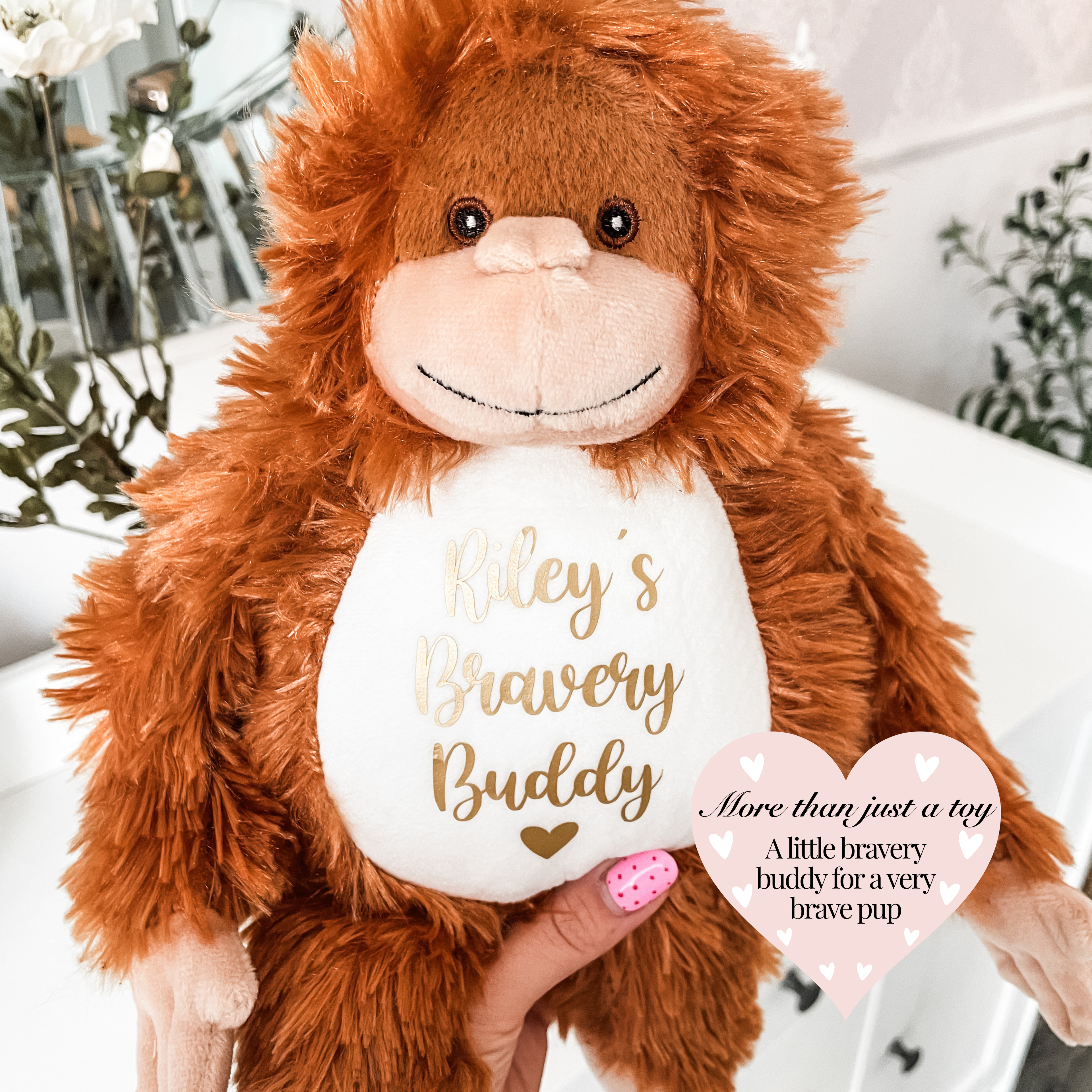 Personalised orangutan dog toy personalised with the dog's name and the words "bravery buddy" underneath in gold text with a heart symbol. Custom dog get well soon gift, soft plush dog toy featuring dog's name.