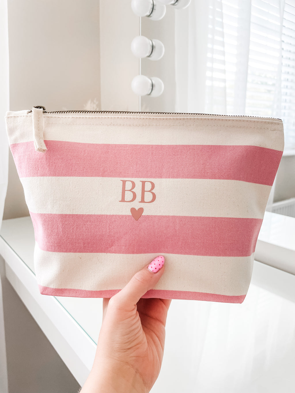 Personalised pink stripe makeup bag with initials and heart design being held to show size, a beautiful cosmetic pouch gift for her.