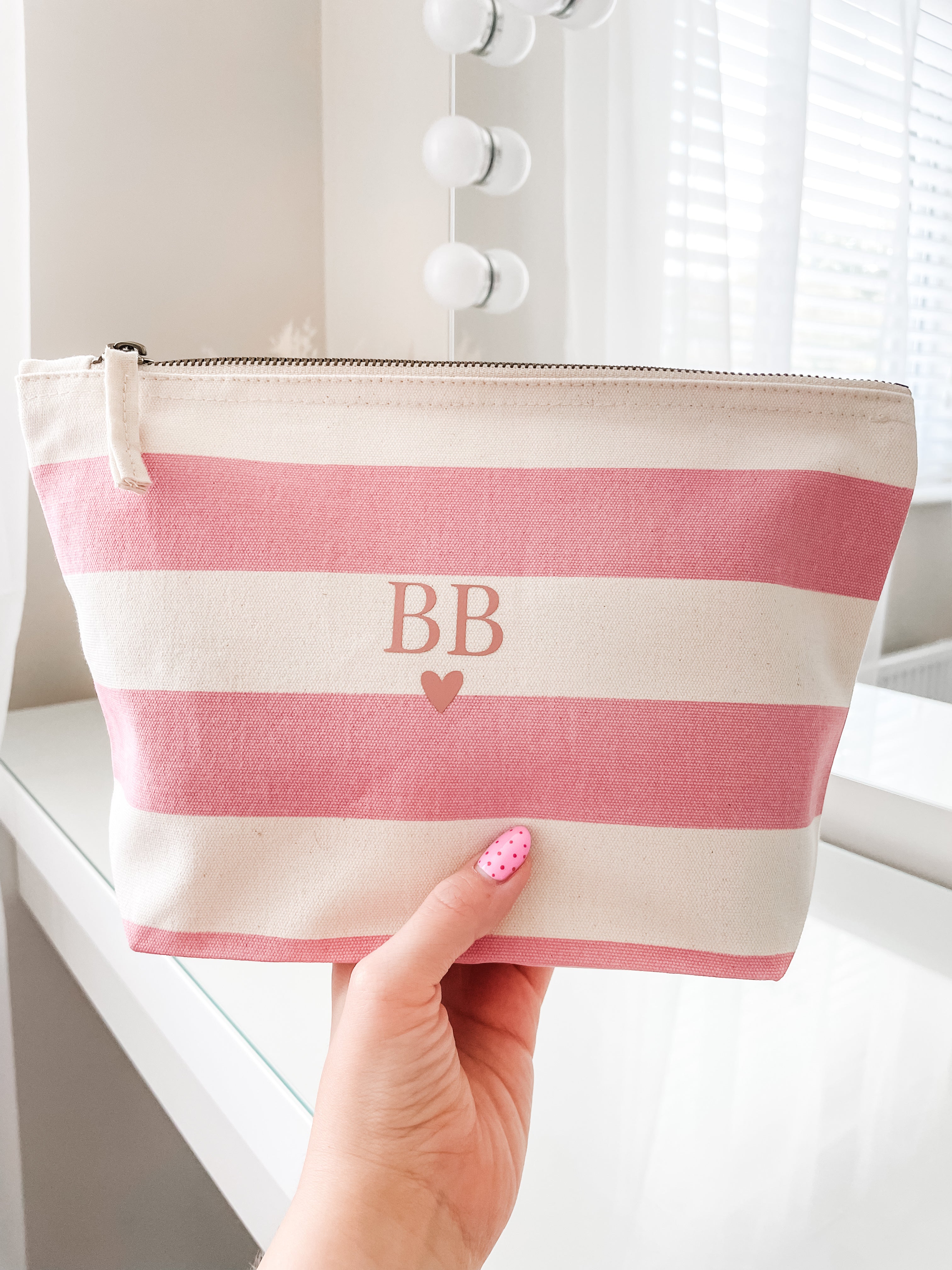 Personalised pink stripe makeup bag with initials and heart design being held to show size, a beautiful cosmetic pouch gift for her.