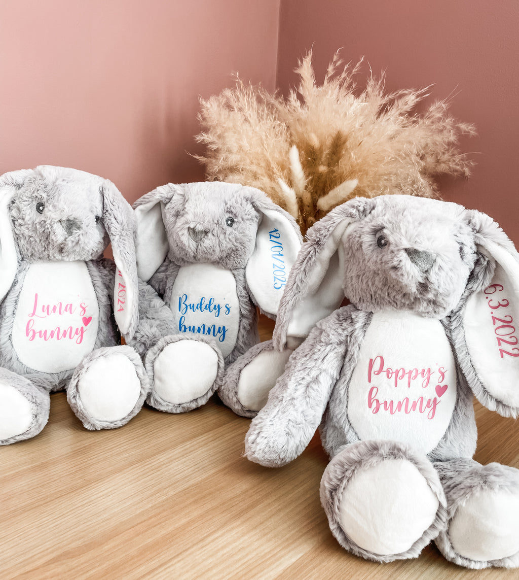Personalised grey bunny dog toys showing custom names and birthday dates in different text colours. Personalised dog name toys.