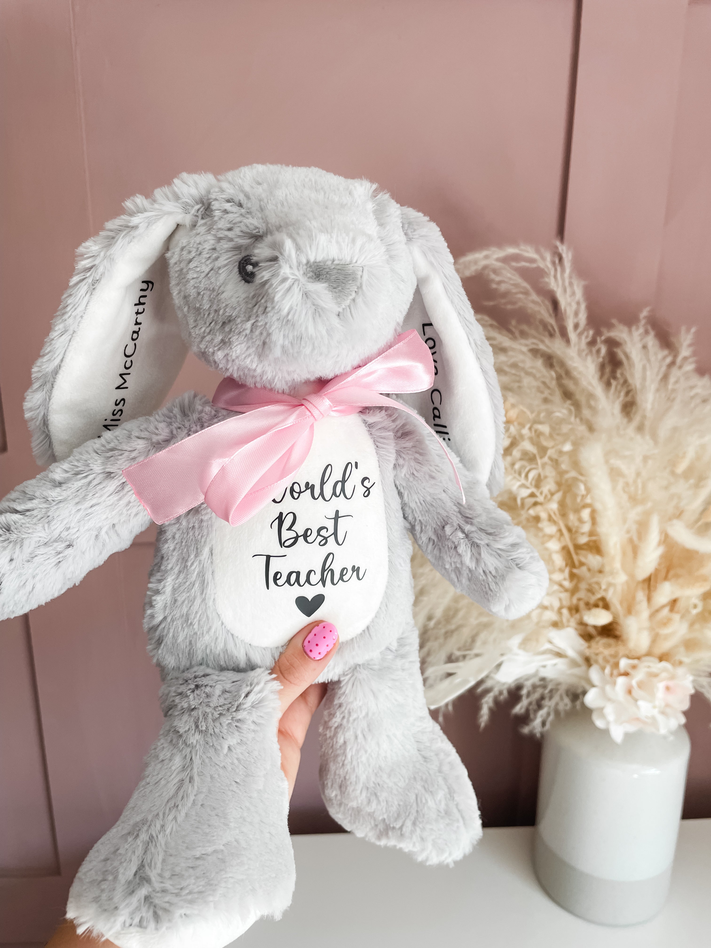 Soft personalised teacher keepsake bunny toy with long floppy ears, a pink satin bow, and a white belly patch that reads 'World's Best Teacher' with a small heart. 